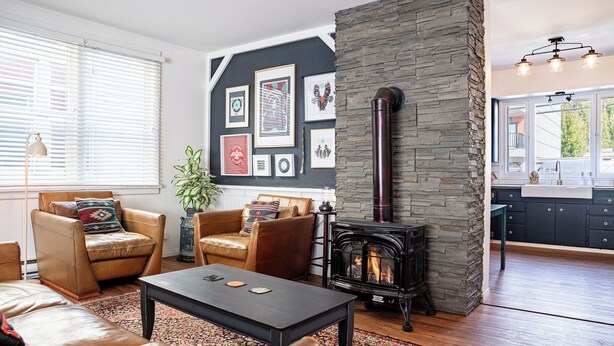 A cozy living room with leather sofas, a coffee table, a fireplace, and a kitchen visible through an open door. - The Downtown Hive by Revelstoke Vacations (Revelstoke)