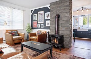 Un salón acogedor con sofás de cuero, una mesita de centro, una chimenea y una cocina visible a través de una puerta abierta.