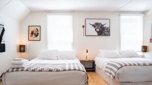 A hotel room with two beds, white bedding, a large window with blinds, a wall-mounted artwork of a bull, and a wall-mounted clock. - The Downtown Hive by Revelstoke Vacations (Revelstoke)
