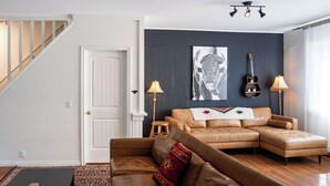 A living room with a sectional sofa, a small stool, a guitar, and a lamp. - The Downtown Hive by Revelstoke Vacations (Revelstoke)