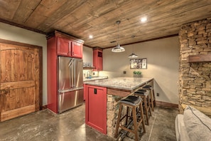 A kitchen with a red refrigerator, wooden cabinets, a stone accent wall, and a bar area.