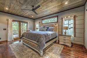 A bedroom with a large bed, a ceiling fan, a nightstand, and a dresser.