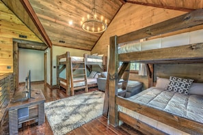 A rustic cabin interior with wooden bunk beds, a television on a wooden stand, and a chandelier.