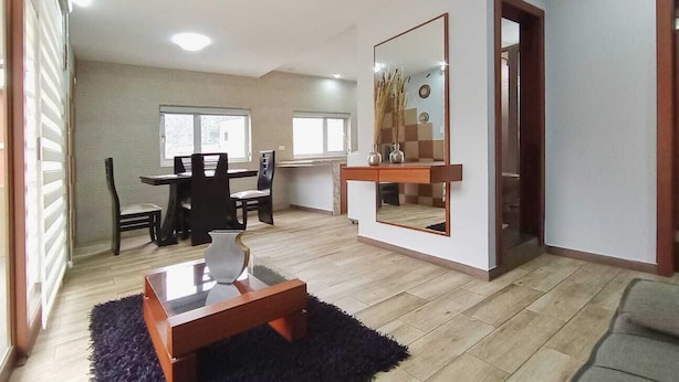 A spacious living area with a wooden floor, a dark blue rug, a coffee table, and a dining area with chairs and a table. - Welcome to your home in Baños (Baños de Agua Santa)