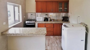 A compact kitchen with wooden cabinets, a gas stove, a microwave, a coffee maker, and a washing machine. - Welcome to your home in Baños (Baños de Agua Santa)