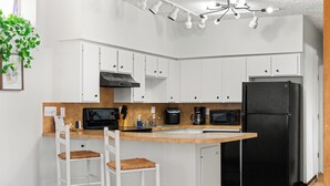 A modern kitchen with white cabinets, a black refrigerator, a coffee maker, and two bar stools.