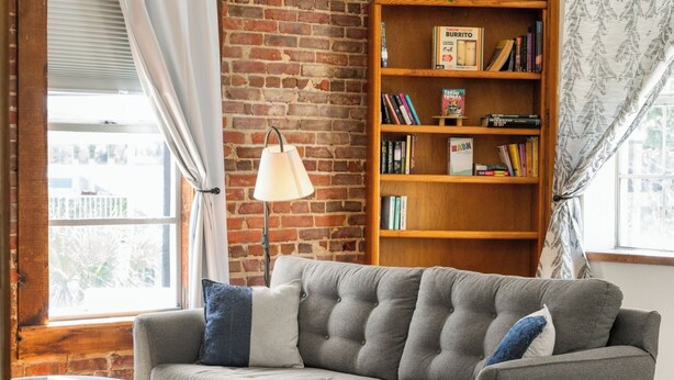 A cozy living room with a grey sofa, a bookshelf, and a lamp.