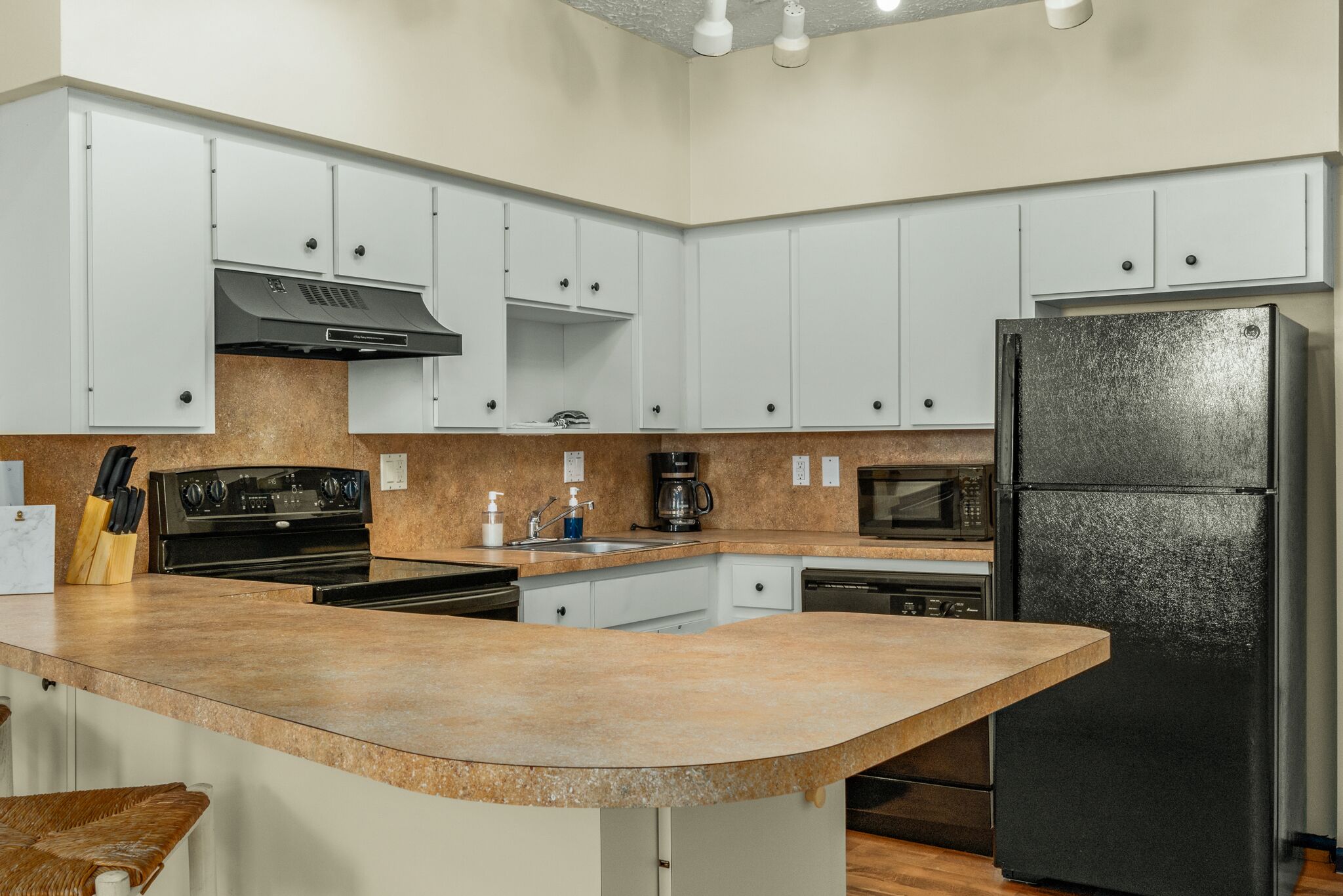 A kitchen with white cabinets, a black refrigerator, a microwave, a stove, and a sink.