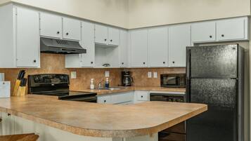 A kitchen with white cabinets, a black refrigerator, a microwave, a stove, and a sink.