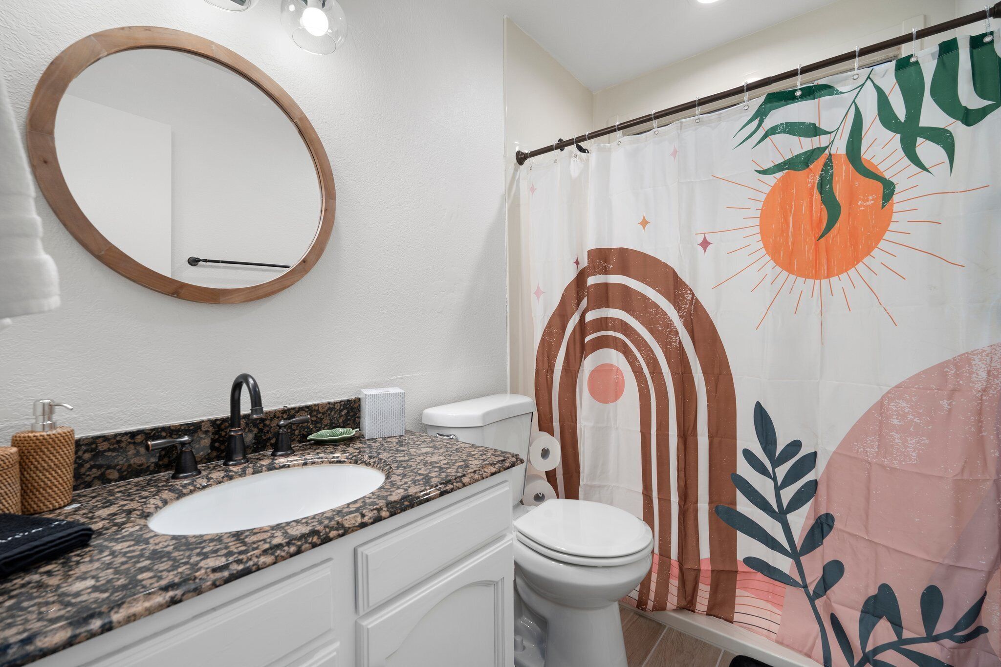 A bathroom with a granite countertop sink, a white toilet, and a shower curtain with a leaf pattern.