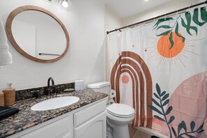 A bathroom with a granite countertop sink, a white toilet, and a shower curtain with a leaf pattern.