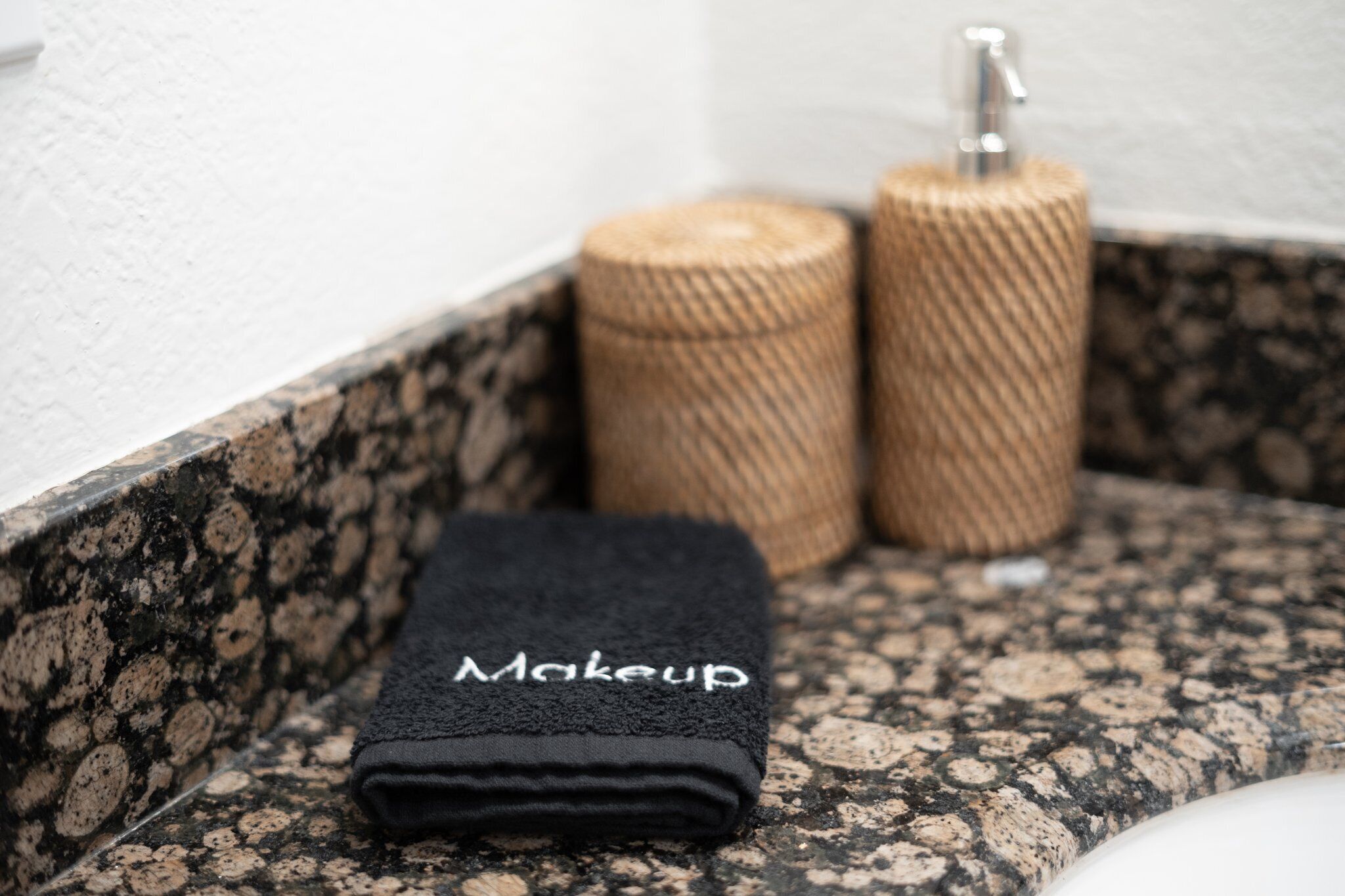 A bathroom with a granite countertop, a black towel labeled "Makeup," and two cylindrical containers.