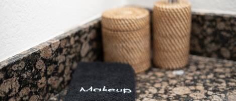 A bathroom with a granite countertop, a black towel labeled "Makeup," and two cylindrical containers.