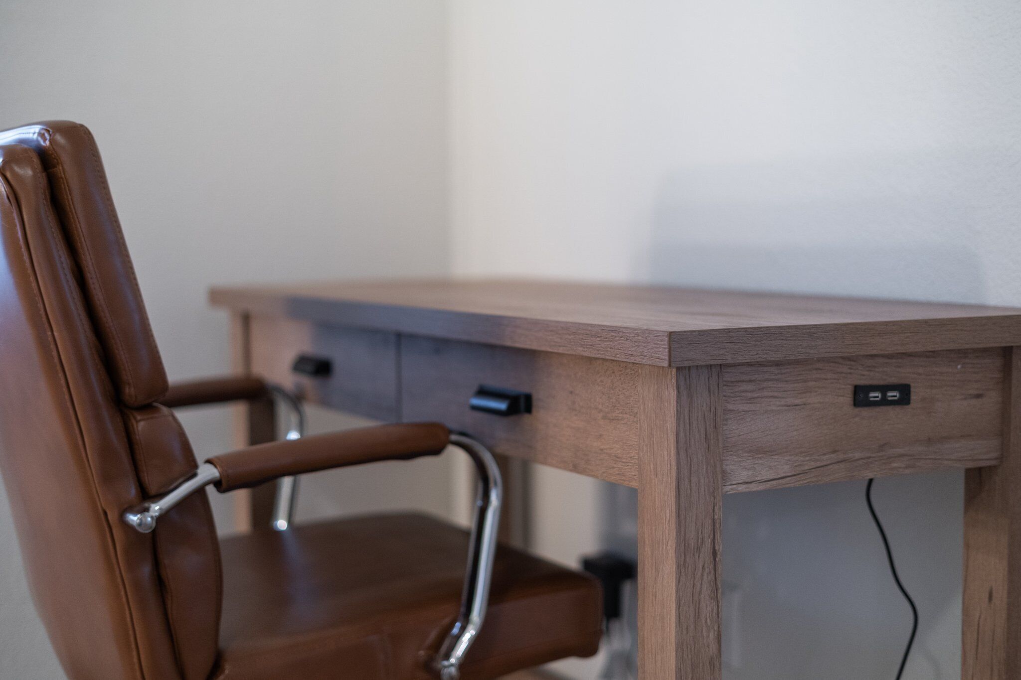 Uma cadeira de couro marrom com apoio de braço de metal e uma mesa de madeira com uma gaveta e um interruptor.