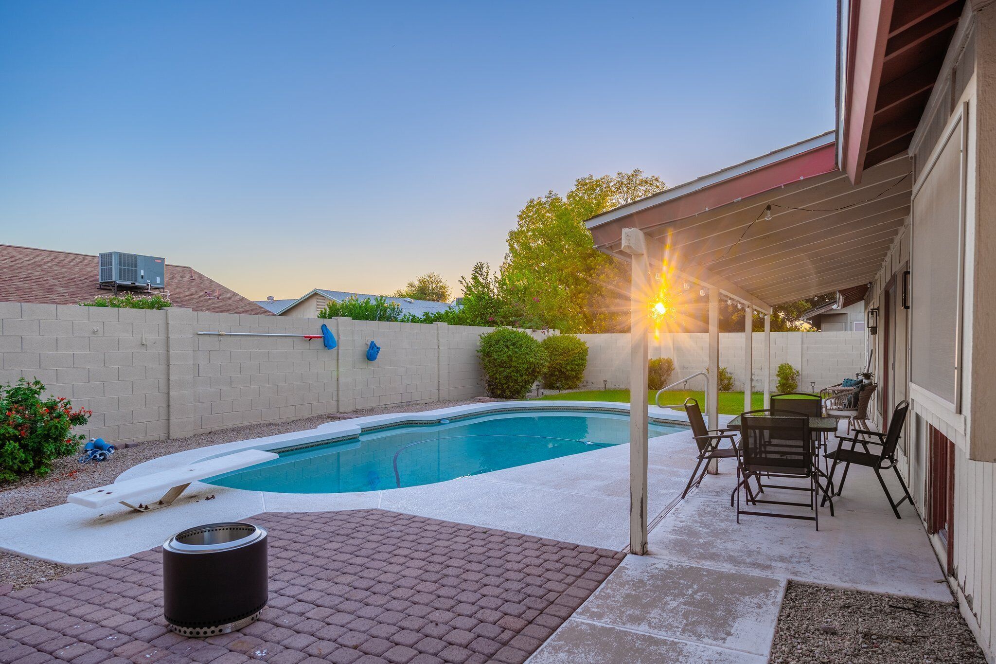 A backyard with a swimming pool, patio furniture, and a covered area with a table and chairs.