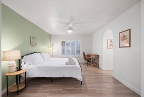 A bedroom with a bed, bedside table, lamp, and a window with blinds.