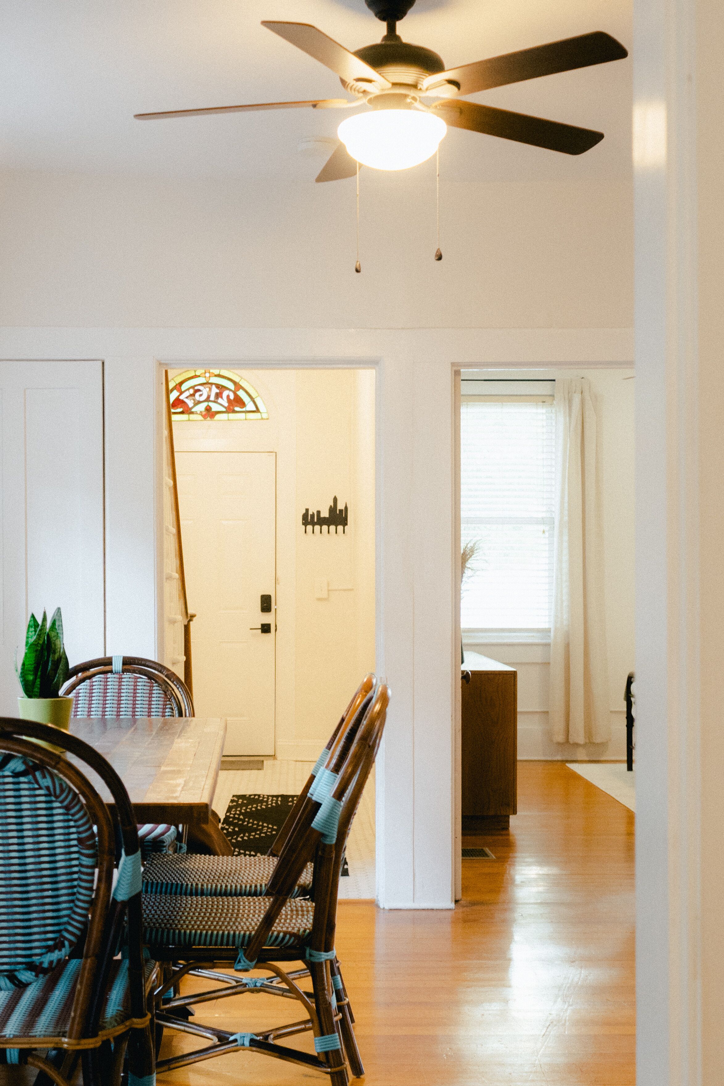 A dining area with a table and chairs, a ceiling fan, and a door with a cityscape sign.