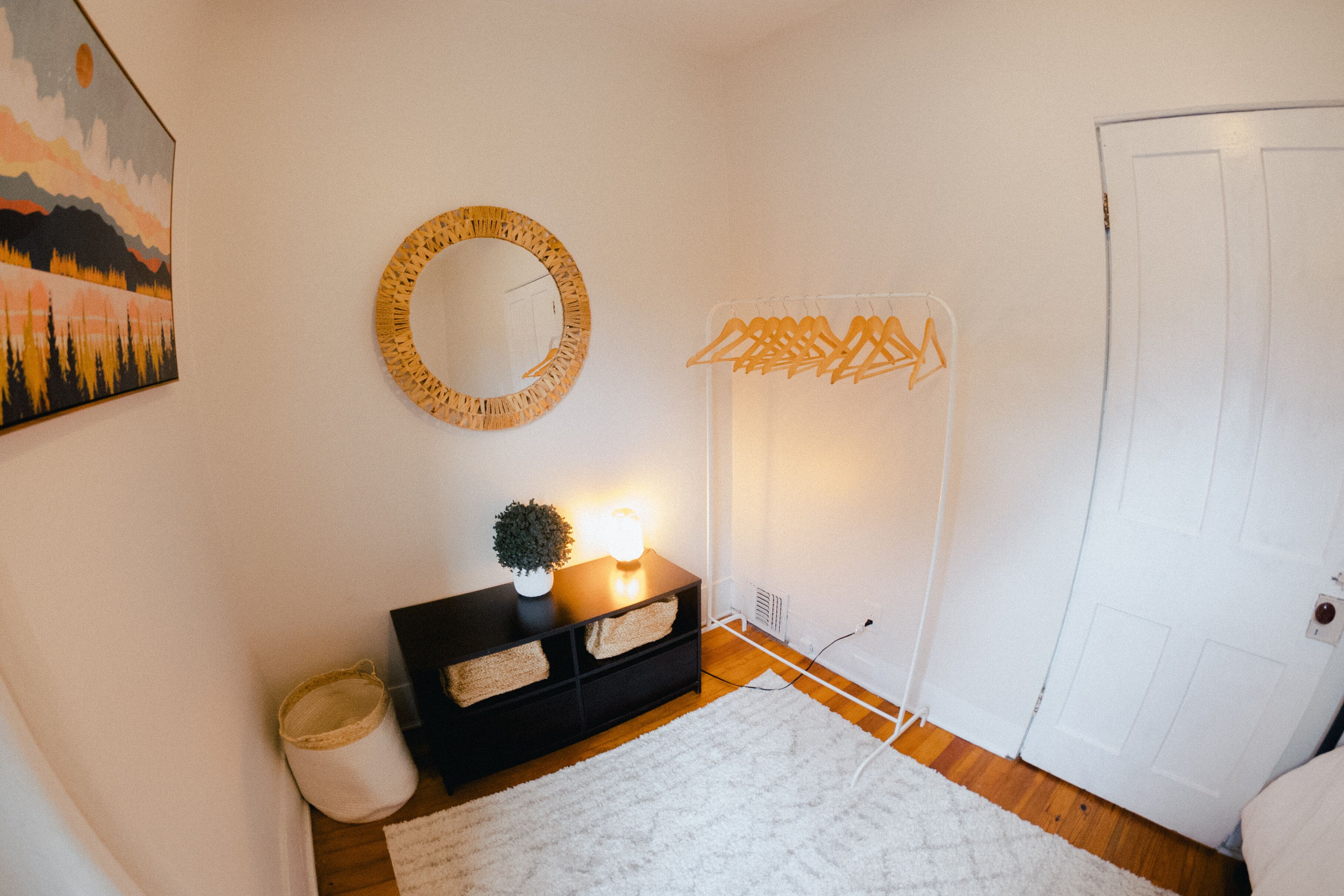 A room with a white door, a black console table with a small plant, a round mirror, and a wall-mounted light fixture.