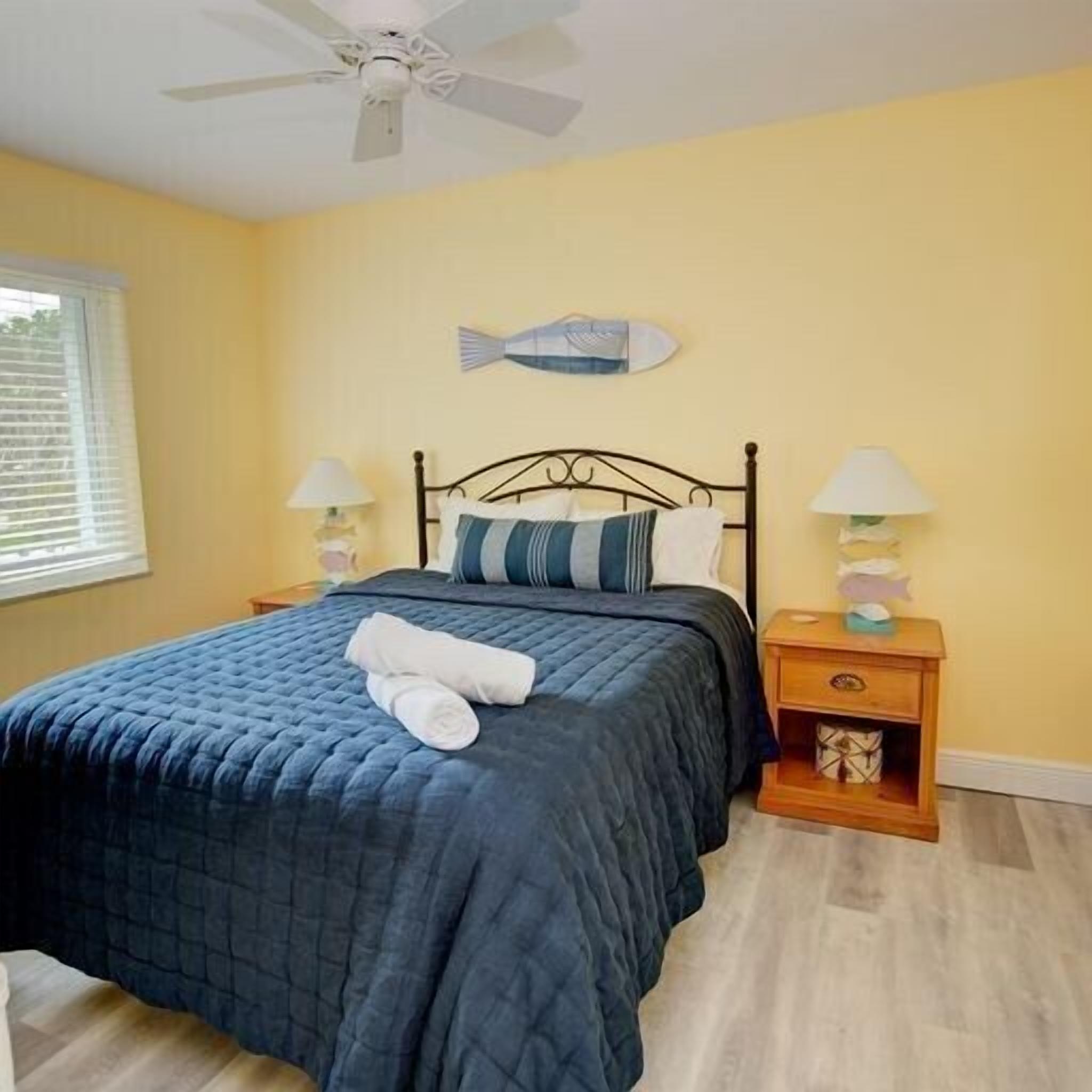 A bedroom with a bed, two bedside tables, a ceiling fan, and a fish-shaped wall decoration.