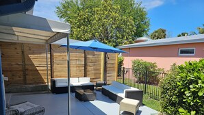 An outdoor patio with wicker furniture, a blue umbrella, and a wooden fence. - In the heart of Stuart-close to beaches (Stuart)