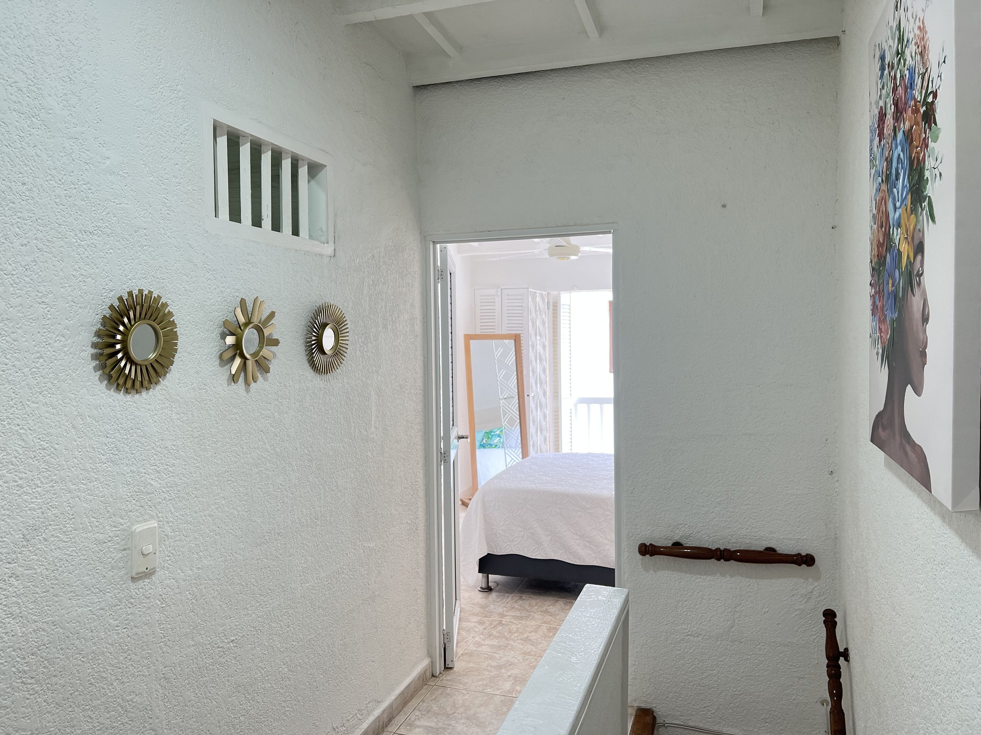 A hallway with white walls, three decorative mirrors, a wooden door, and a ceiling fan.