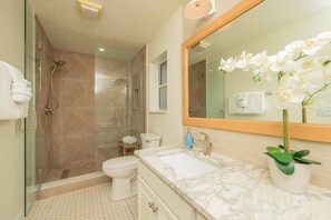 Une salle de bain moderne dotée d’une douche à parois de verre, de toilettes, d’un lavabo avec un plan de toilette en marbre et d’un grand miroir.