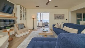 Ein Wohnzimmer mit Fernseher, Deckenventilator, Sofa, Couchtisch und Blick ins Freie.