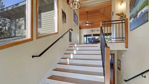 Eine Treppe mit Holzstufen und Geländer, die zu einem Bereich im zweiten Stock führt, mit Deckenventilator und einem Schild mit der Aufschrift 'SKI LODGE'.