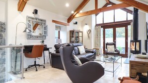A spacious living area with a modern sofa, a glass coffee table, and a leather armchair. A fireplace is visible, suggesting a cozy atmosphere. - Pol Glas Hall (Helston)