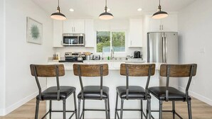 Une cuisine moderne avec des meubles blancs, des appareils en acier inoxydable et quatre chaises en bois dotées de sièges en cuir noir.