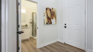Un couloir avec un plancher en bois, une porte blanche et une salle de bain visible au fond.