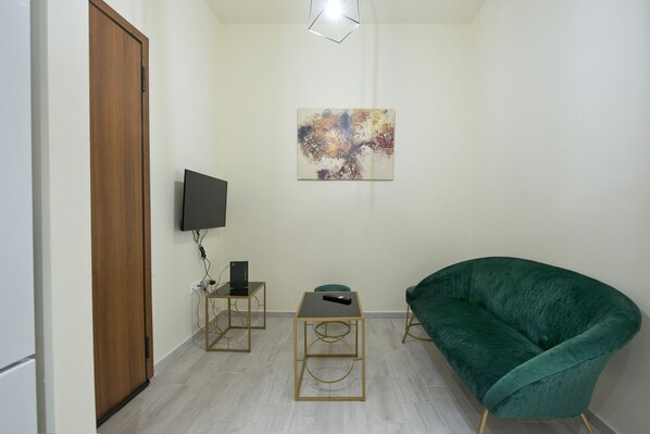 Un petit salon moderne, avec un fauteuil vert, un téléviseur à écran plat fixé au mur et une petite table sur laquelle repose une télécommande.