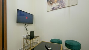 A room with a flat-screen TV mounted on the wall, a small table with a remote control, and two green cushioned stools. - Koukaki Gem Cozy 1BR Renovated Apt near Center (Athina)