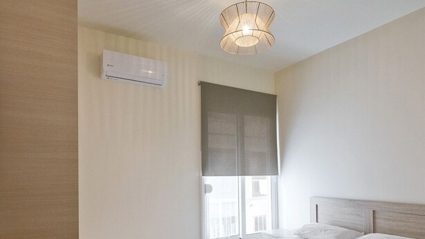 A hotel room with a large bed, a wooden floor, a ceiling light fixture, and a window with a view of buildings. - Koukaki Gem Cozy 1BR Renovated Apt near Center (Athina)