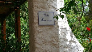 Una señal en una pared blanca que dice "Villa Francesca" en un jardín.