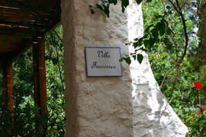 Una señal en una pared blanca que dice "Villa Francesca" en un jardín.
