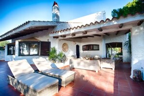 Una casa con un patio que incluye dos tumbonas y una zona de estar cubierta.