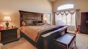 Une chambre à coucher avec un grand lit, des tables de chevet, un bureau, une chaise, un ventilateur de plafond et une fenêtre avec des rideaux.