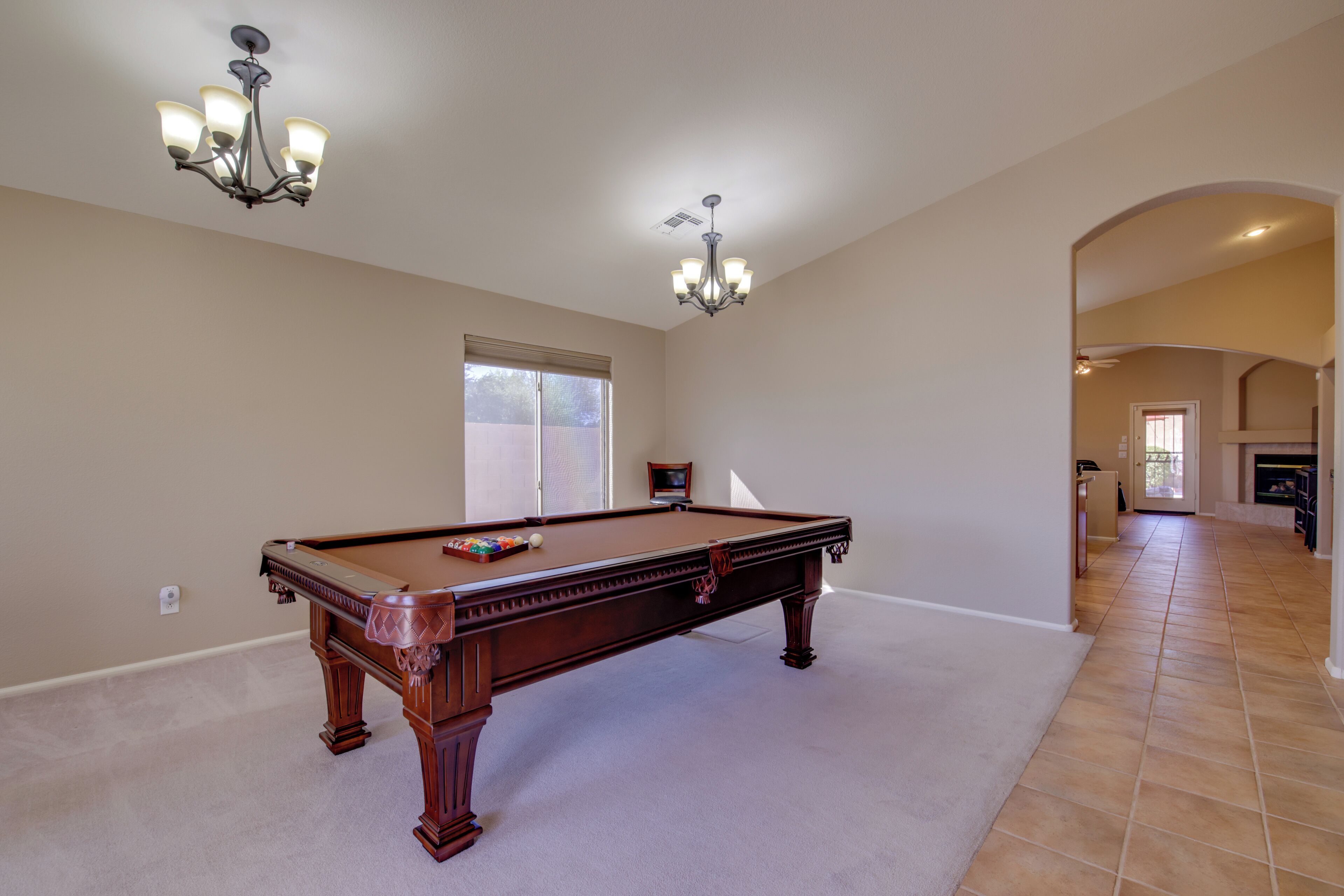 A spacious room with a pool table, a chandelier, and a fireplace.
