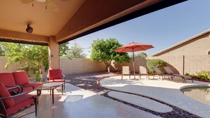 Une terrasse extérieure couverte avec une piscine, des chaises rouges et un parasol rouge.