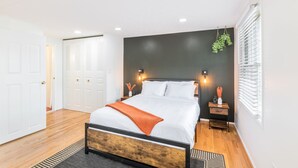 Camera da letto moderna con un letto grande, testiera in legno, biancheria da letto bianca e una parete d'accento scura.