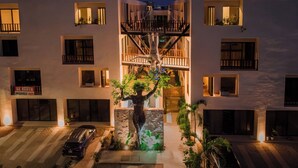 A modern multi-story building with balconies, a central staircase, and a sculpture in the courtyard. - Smart Depas Tulum (Tulum)