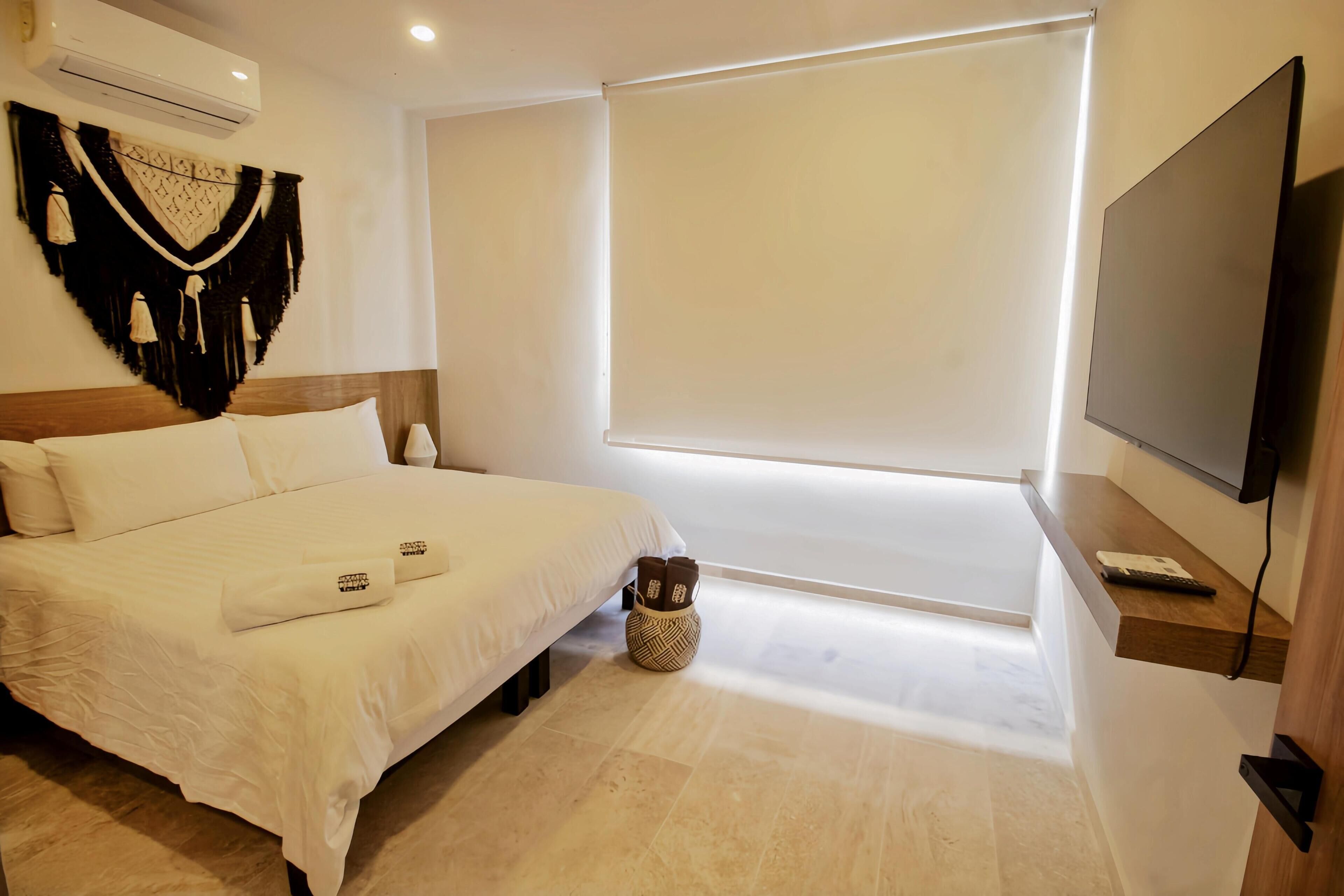 A hotel room with a bed, a wall-mounted TV, a large window, and a decorative wall hanging.