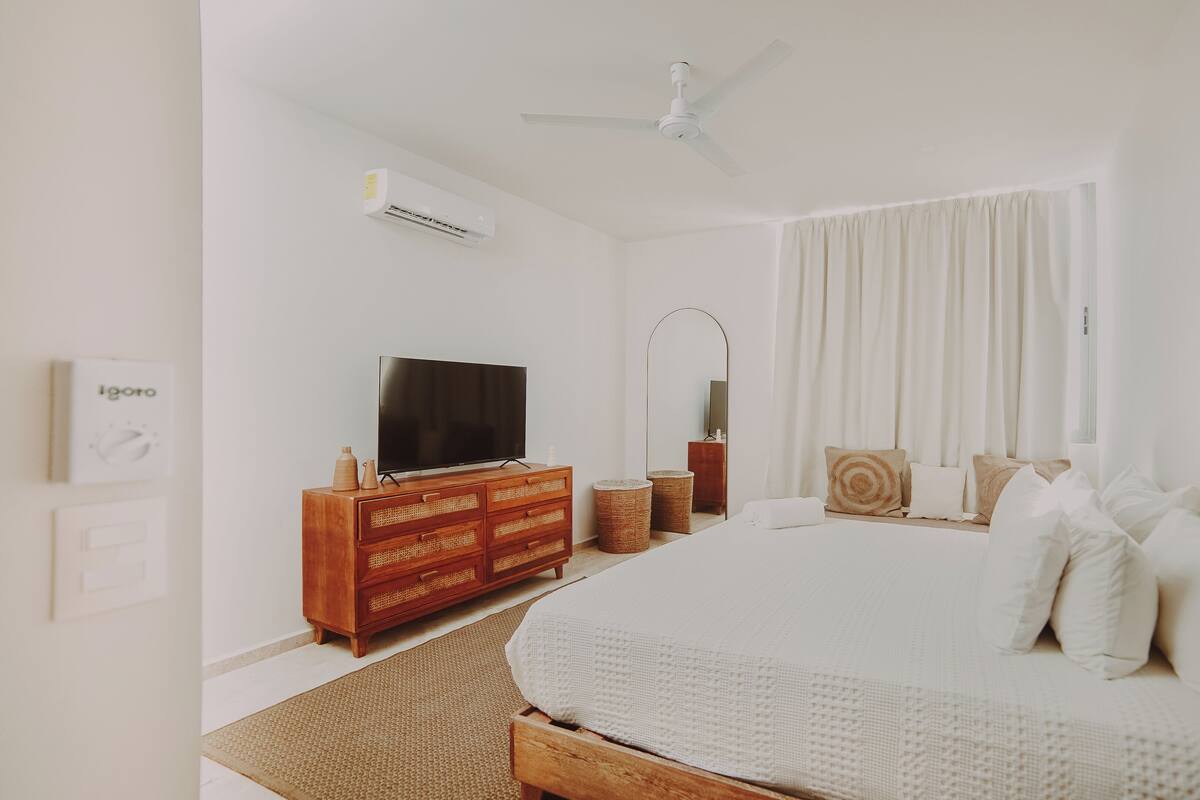 A bedroom with a bed, a TV, a ceiling fan, and a wall-mounted air conditioner.