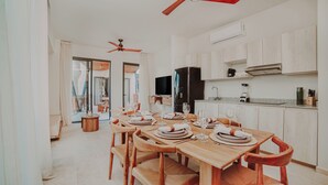 A dining area with a wooden table set for four, a ceiling fan, a black refrigerator, and a kitchen counter with a blender. - Smart Depas Tulum (Tulum)