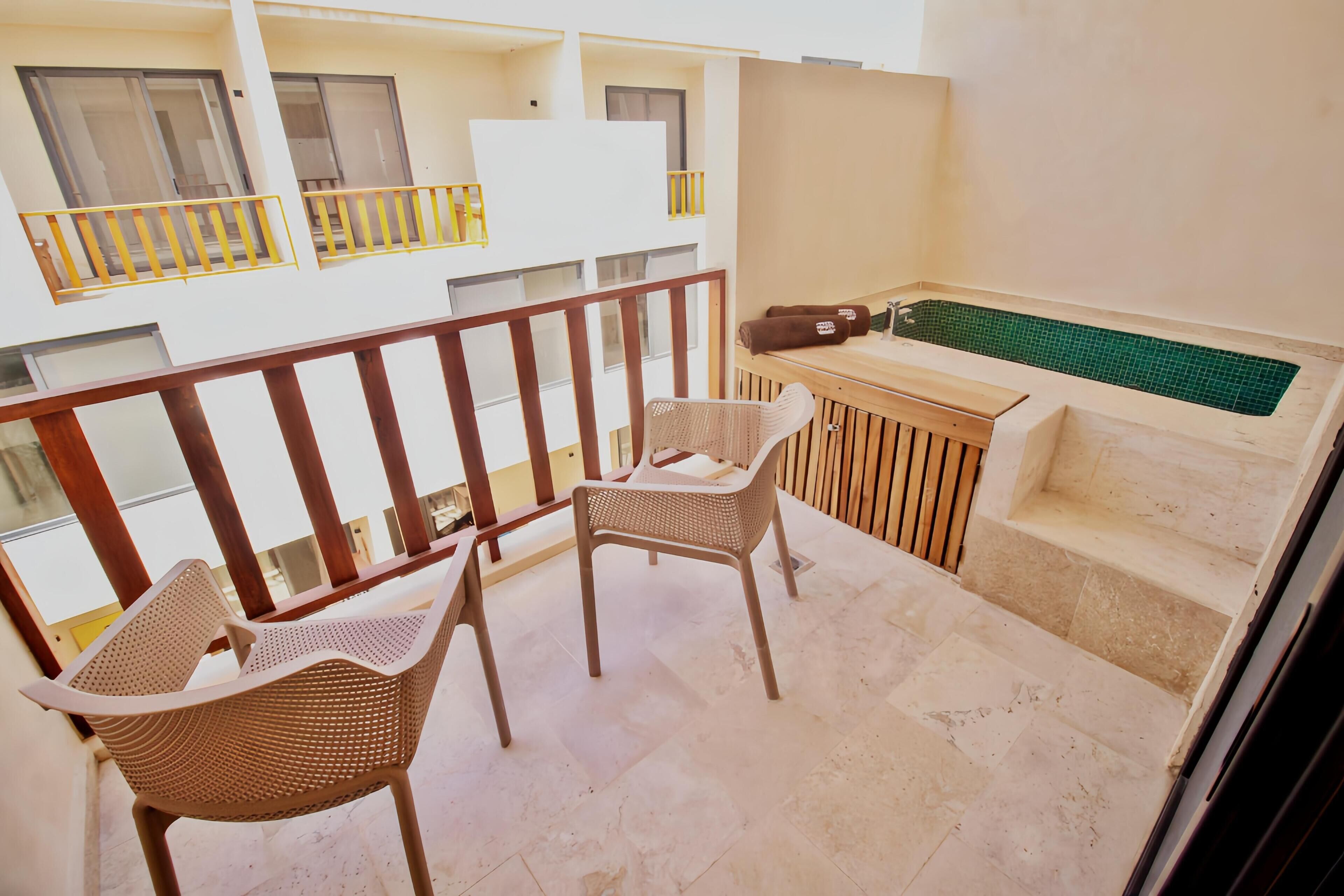 A balcony with two wicker chairs, a small table, a bench, and a green-tiled pool.