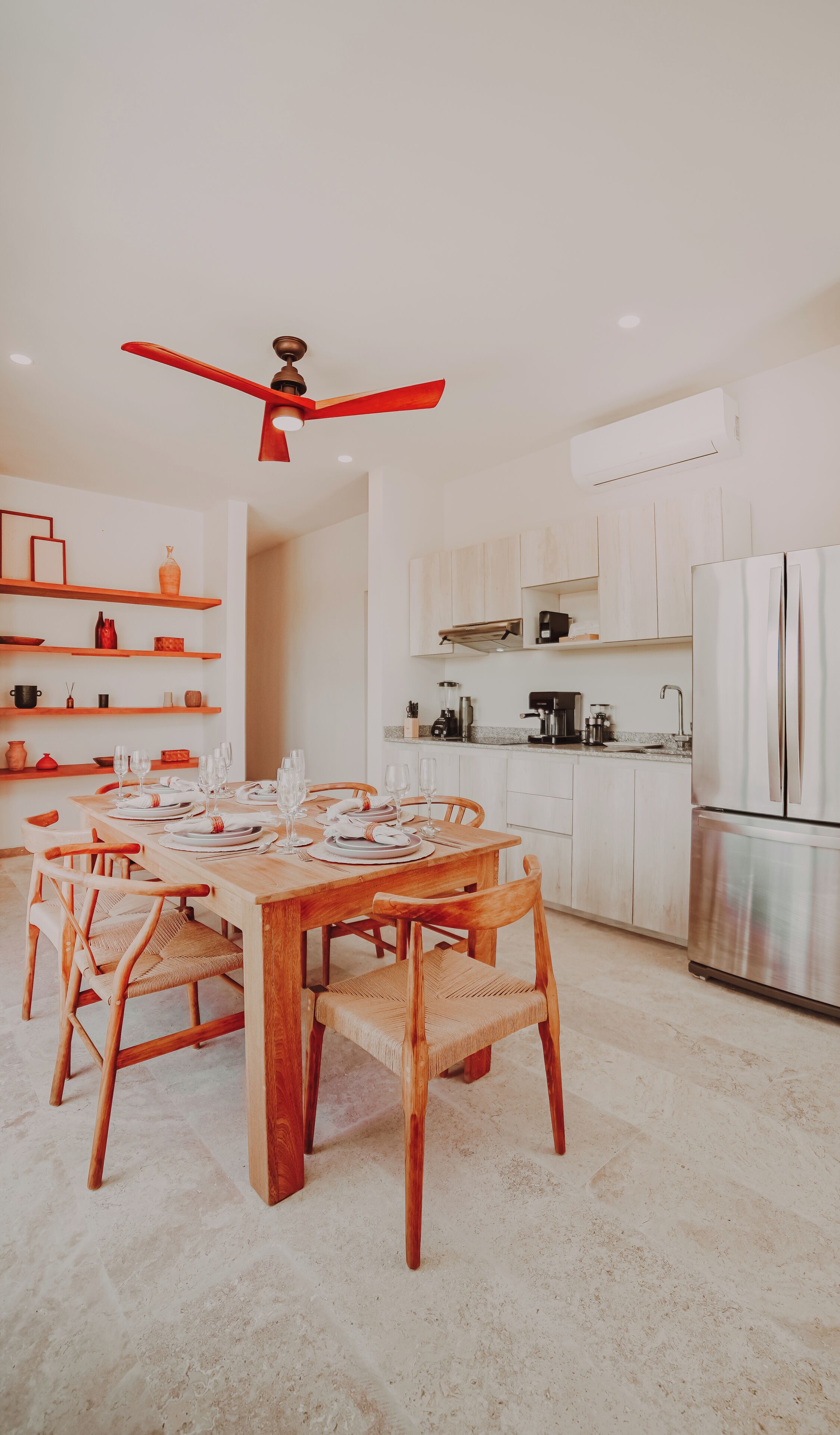 A modern kitchen with white cabinets, a wooden dining table, and a ceiling fan.