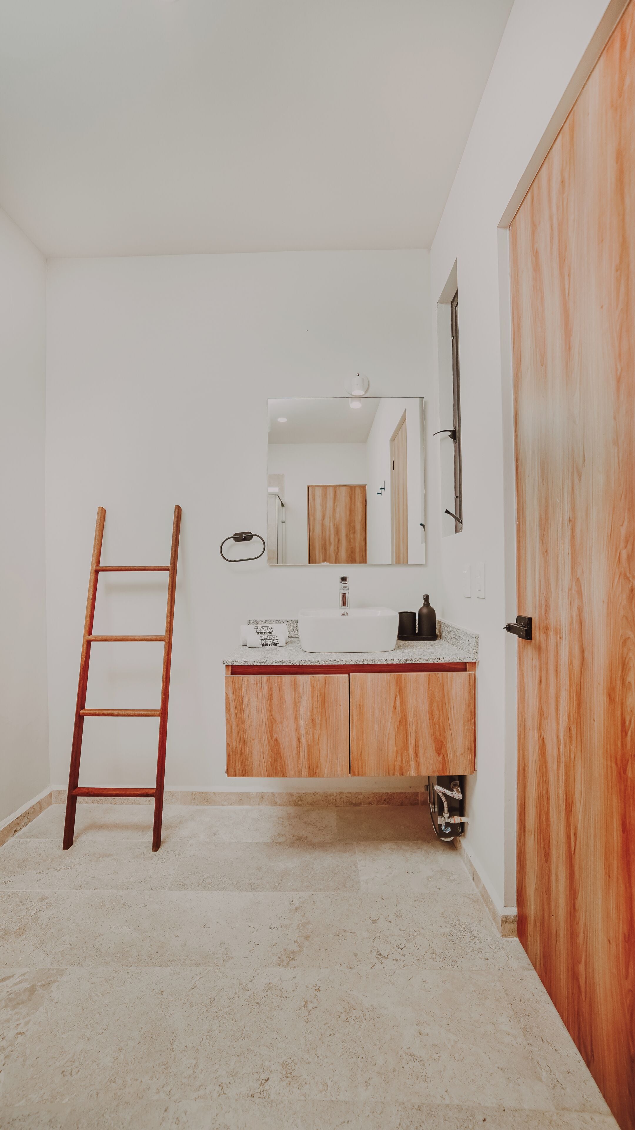A bathroom with a wooden ladder, a sink with a mirror, and a wooden door.