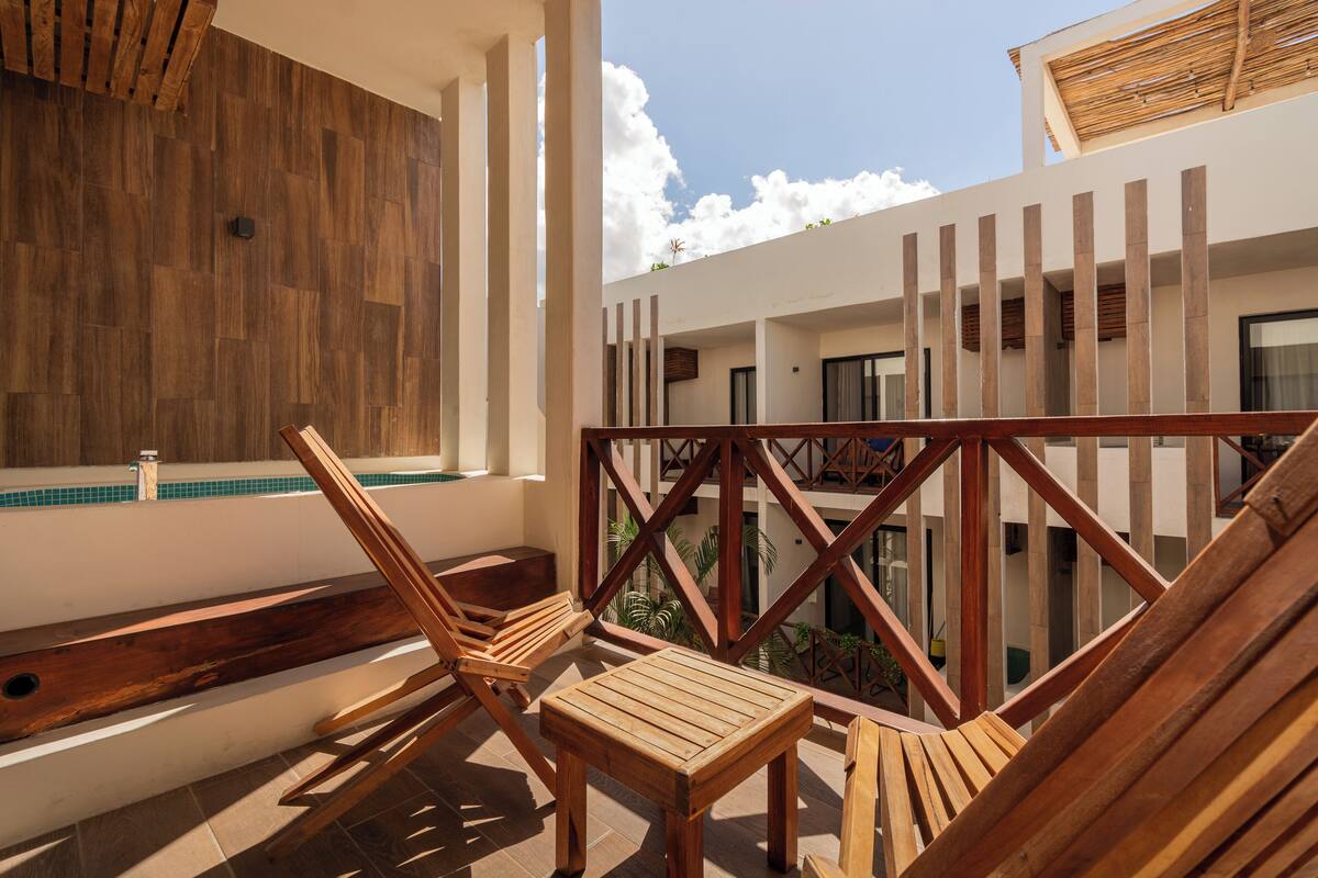 A wooden deck with two lounge chairs and a small table, overlooking a pool and a building with a modern design.