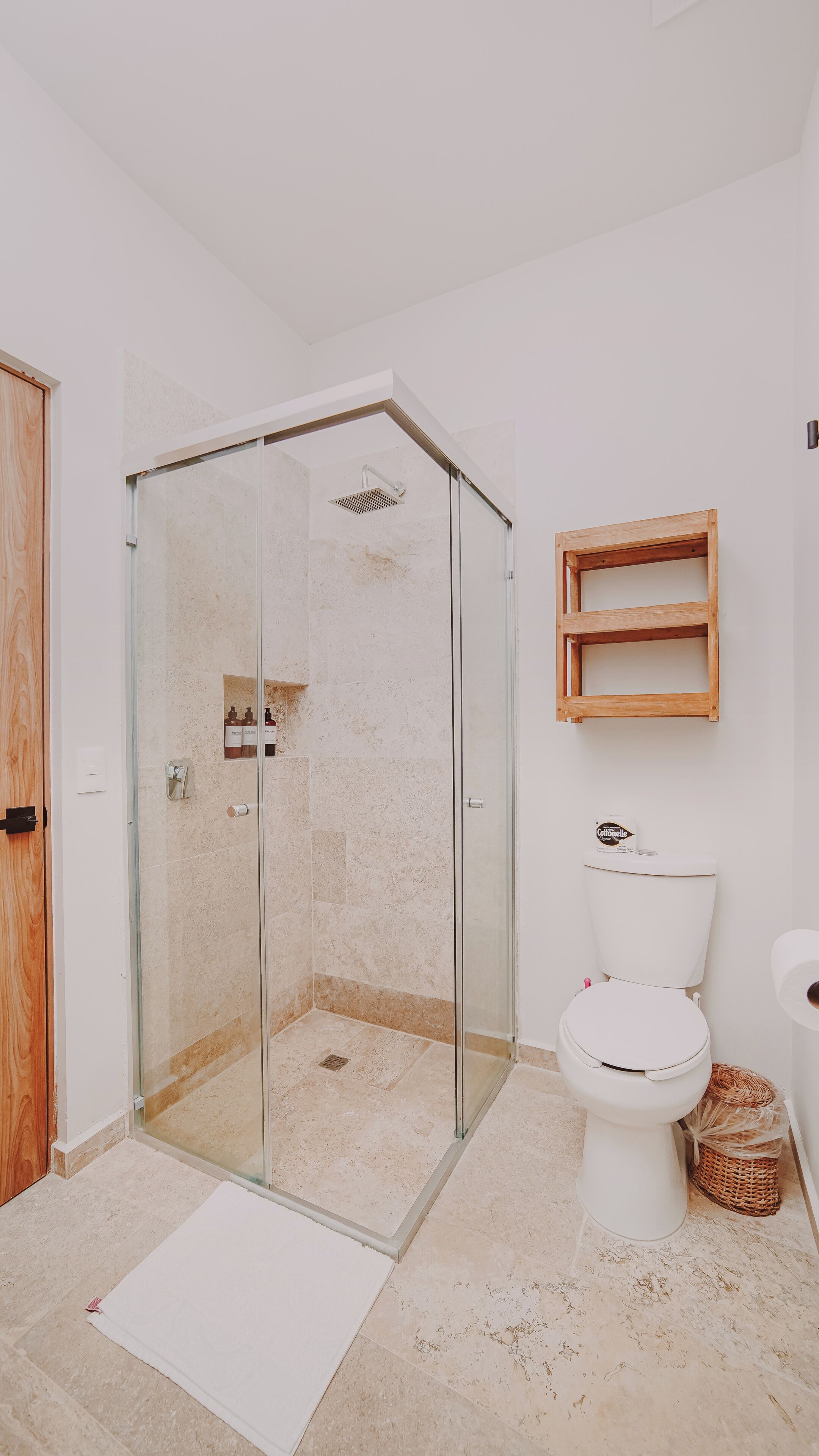 Une salle de bain avec une douche à parois de verre, des toilettes et une étagère en bois.